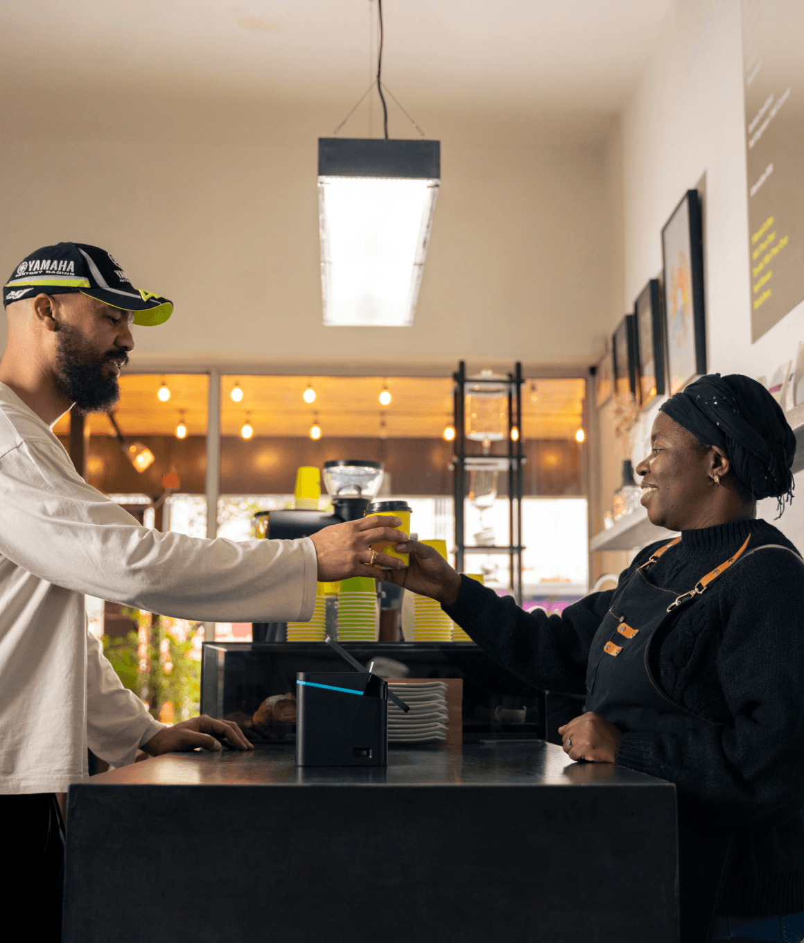 A man and a woman are exchanging an item at a Coffee shop counter in a bright, modern office setting.